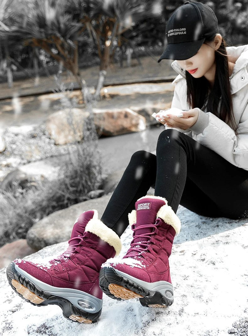 Model zittend met bordeauxrode snowboots op besneeuwde rots